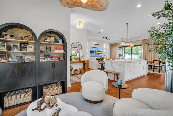 Open-concept living space featuring wood-finish flooring, a contemporary kitchen island with a waterfall countertop, and an arched built-in shelving unit