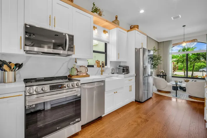 Modern kitchen featuring white cabinetry with brass hardware, stainless steel appliances, a farmhouse sink, and wood-finish flooring