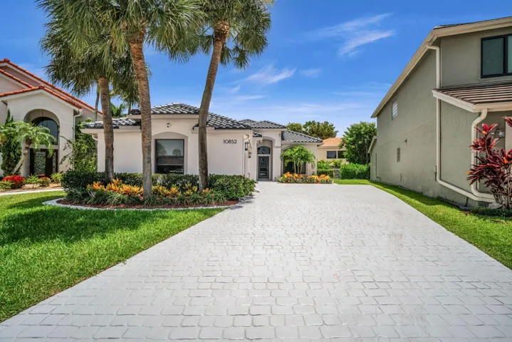 Exterior showcasing a paver driveway, mature palm trees, sculpted landscaping, a tiled roof, and a prominent arched entryway