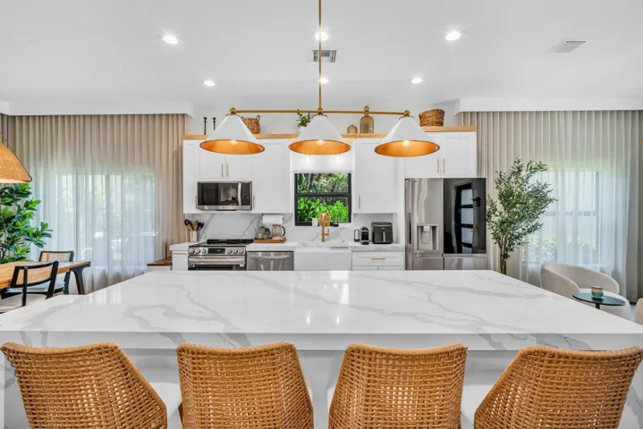 Expansive kitchen island with a white veined countertop, featuring white cabinetry, stainless steel appliances, and brass-finish pendant lighting
