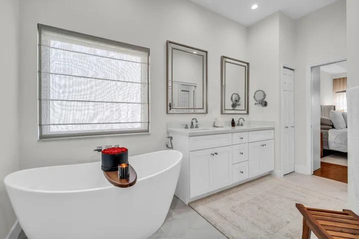 Freestanding soaking tub with a wall-mounted faucet, dual vanity with a light-colored countertop, framed mirrors, and recessed lighting