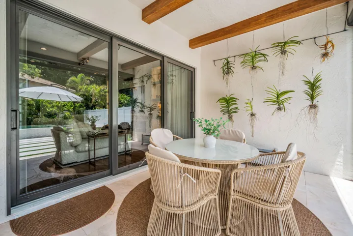 Covered patio featuring exposed wood beams, a textured white wall with suspended plants, and light-toned tile flooring
