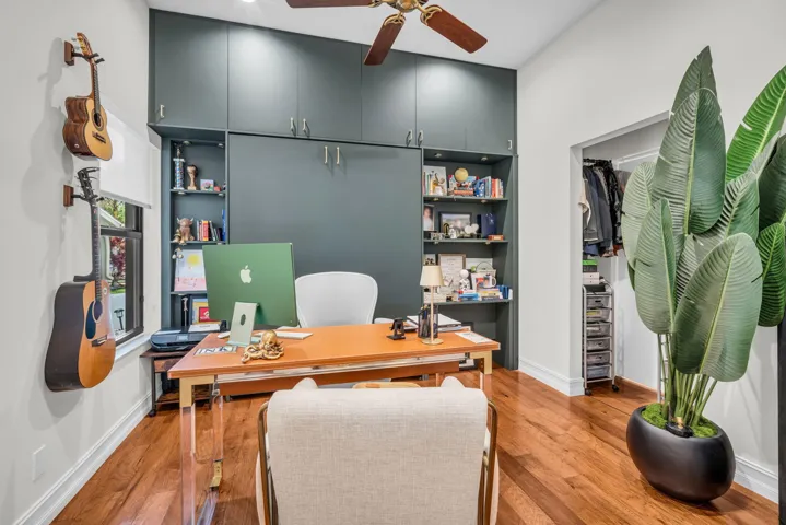 Dedicated room featuring extensive built-in cabinetry, integrated shelving, wood-finish flooring, a ceiling fan, and a functional window