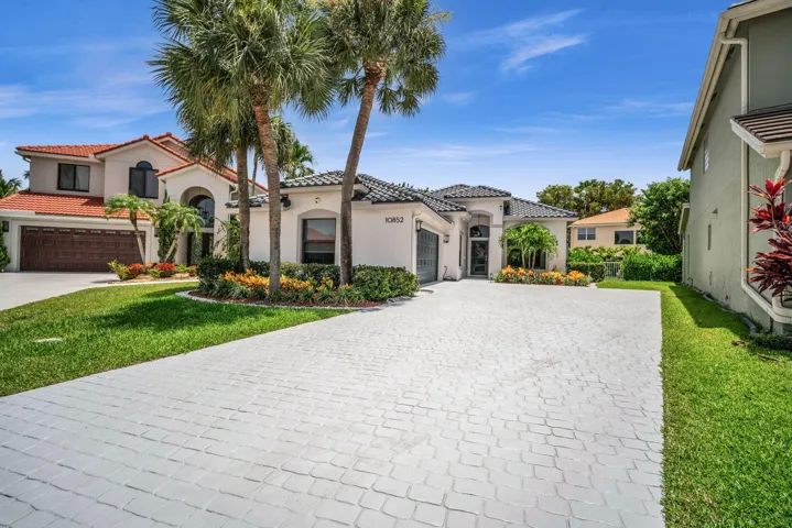 Contemporary stucco exterior with a tiled roof, featuring a paver driveway, mature palm trees, and established landscaping