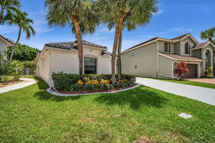 Exterior featuring a tile roof, stucco finish, arched window, tropical landscaping with palm trees, and a paved driveway