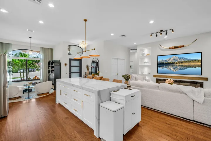 Spacious living area featuring wood-finish flooring, a white kitchen island with a stone-finish countertop, and a built-in fireplace with a wood mantle