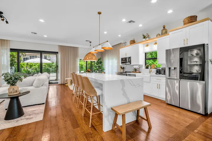 Open-concept kitchen featuring a waterfall island with integrated seating, white cabinetry with gold-tone hardware, and wood-finish flooring