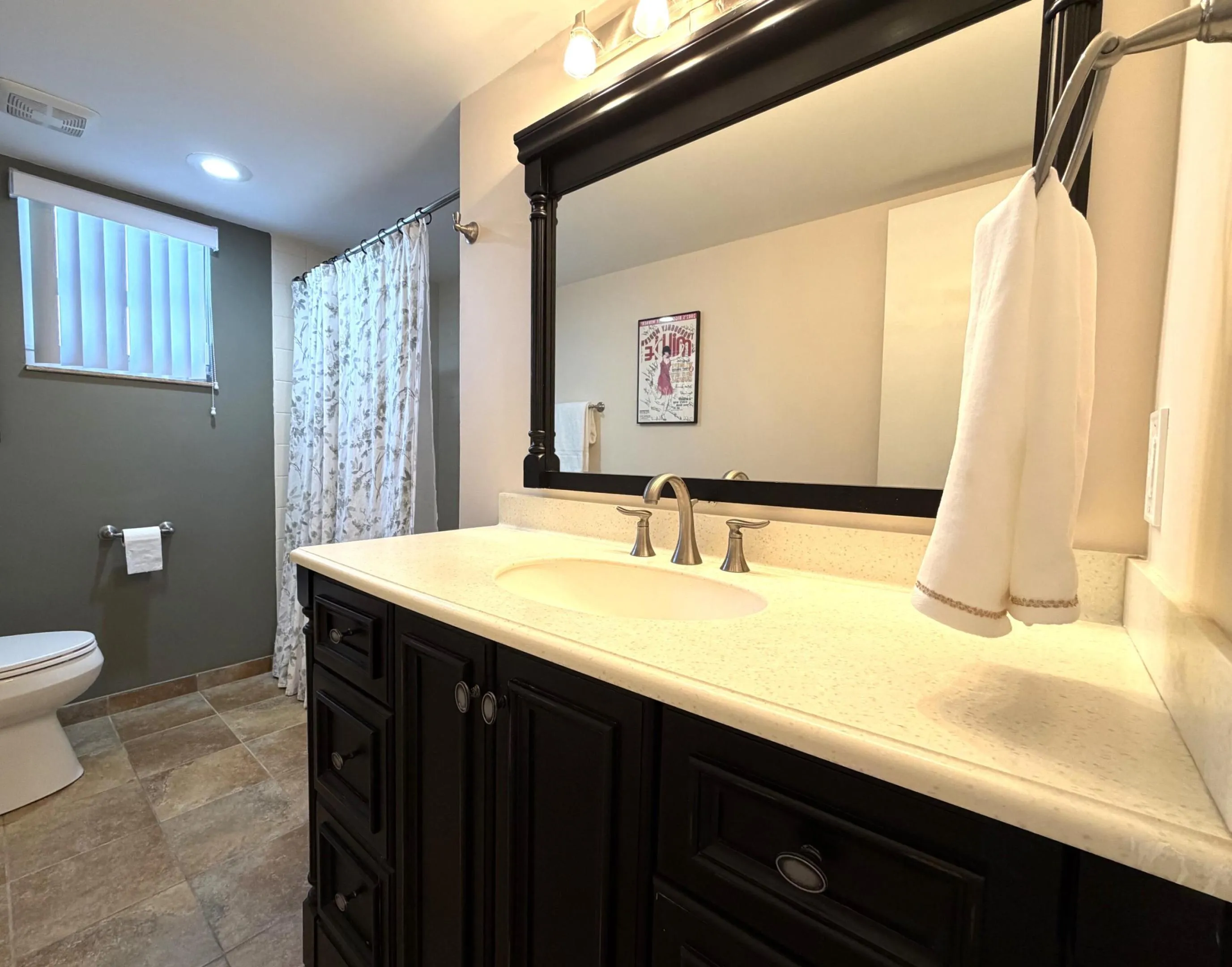 Bathroom featuring a dark wood vanity with a light-toned countertop, a large framed mirror, and a brushed nickel faucet