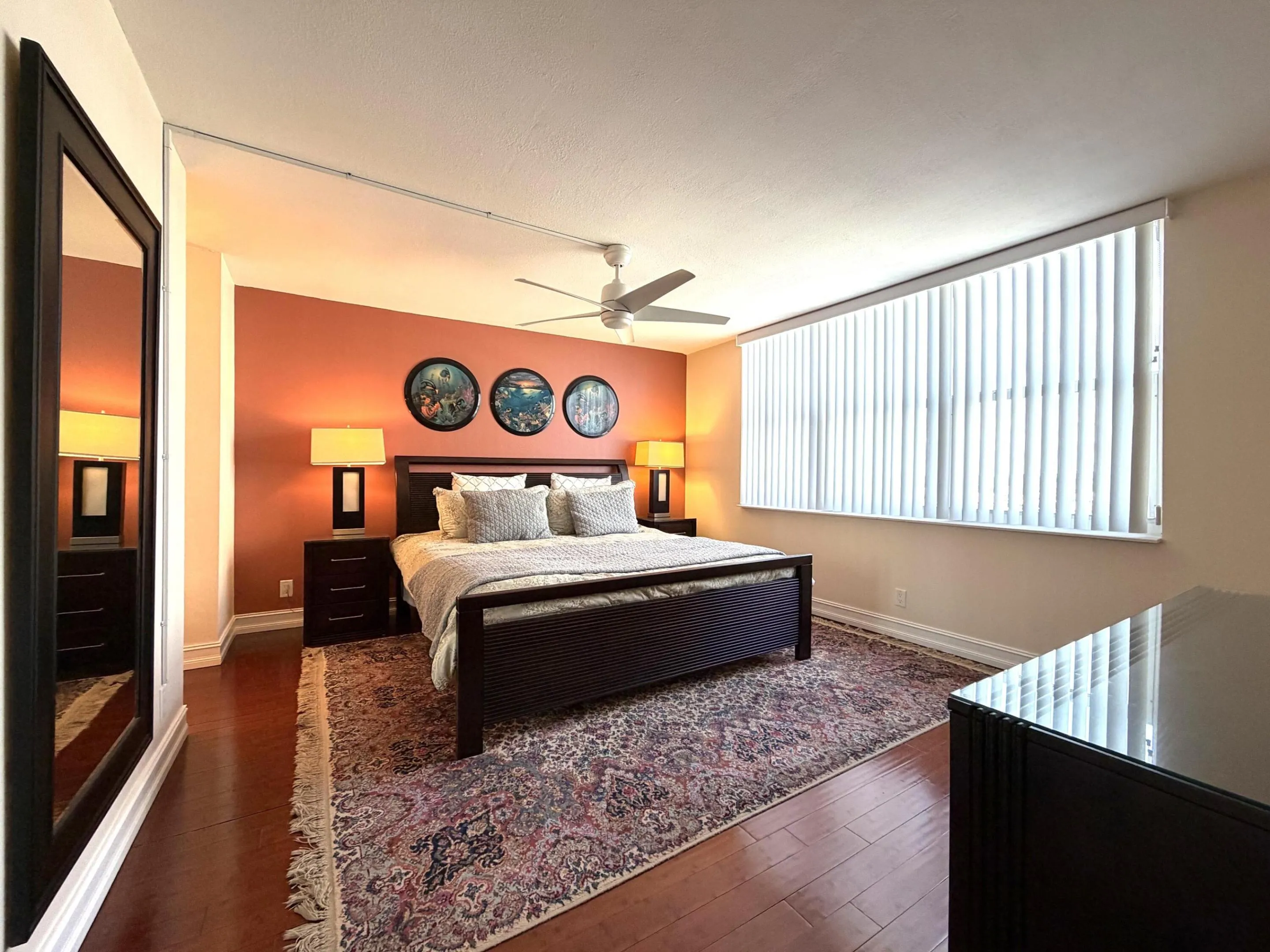 Spacious room featuring wood-finish flooring, a full-wall window with vertical blinds, a ceiling fan, and painted accent walls