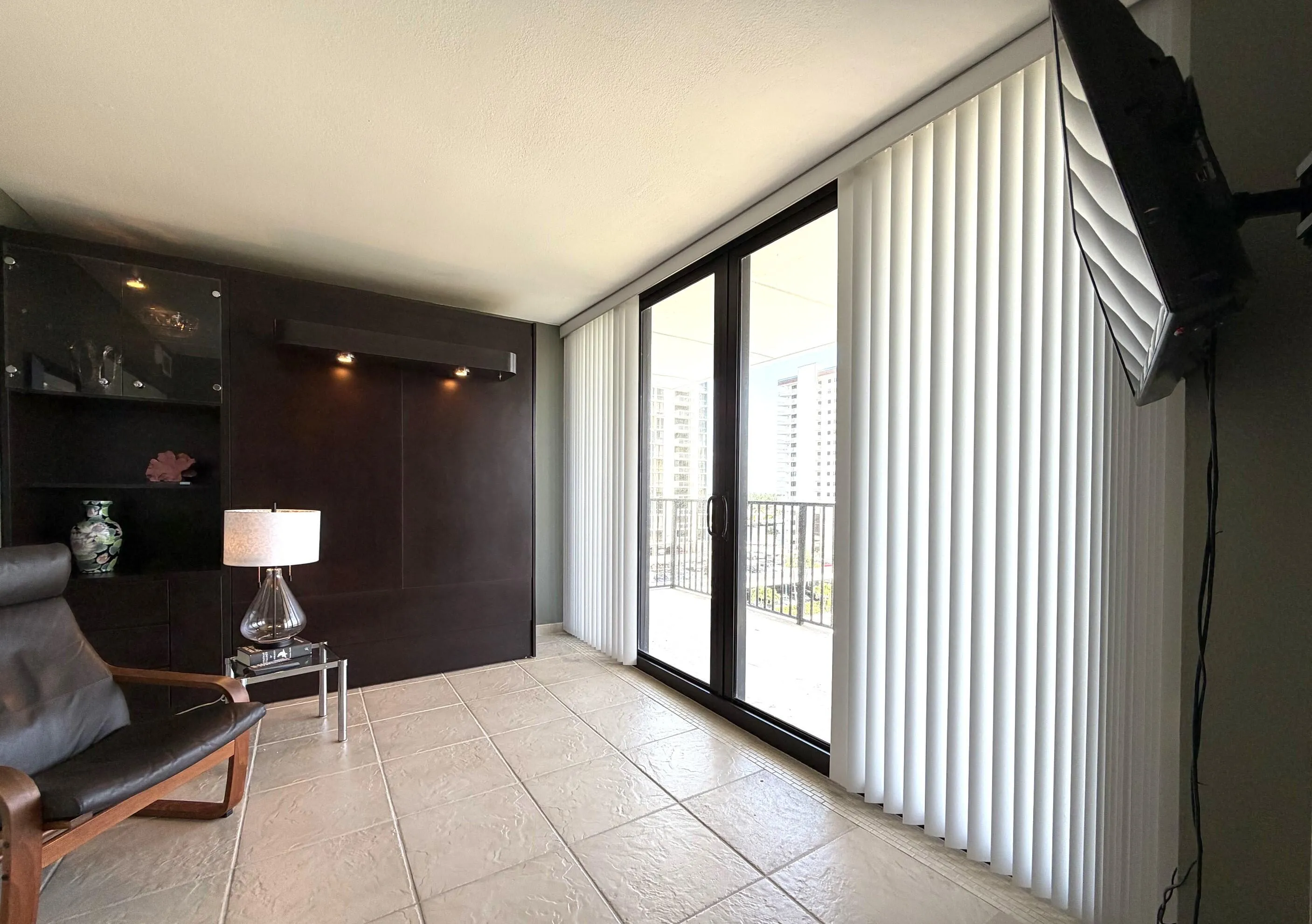 Glass sliding doors with vertical blinds, textured square tile flooring, and a built-in wall unit with display shelving and accent lighting