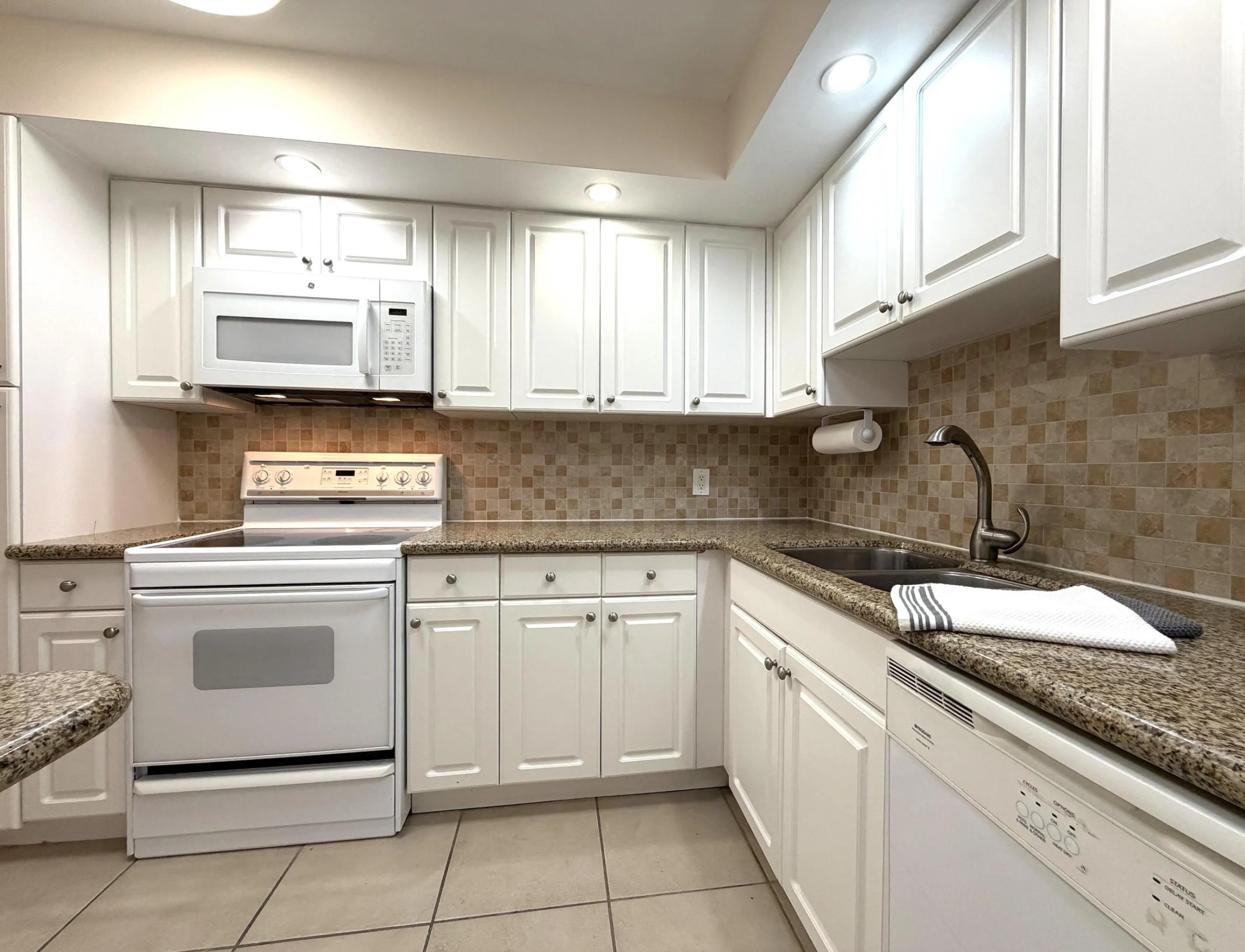 Kitchen featuring white cabinetry, speckled countertops, a mosaic tile backsplash, a built-in microwave, and a white electric range
