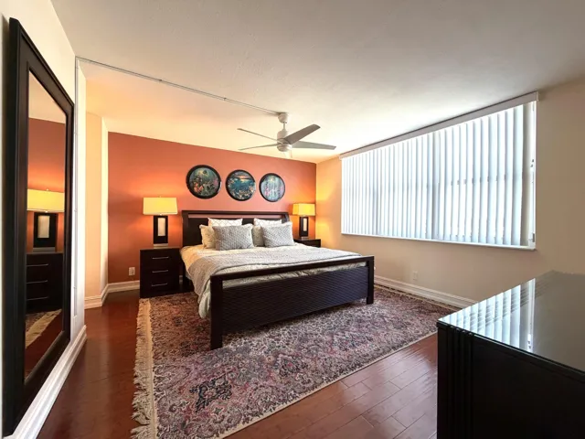 Spacious room featuring wood-finish flooring, a full-wall window with vertical blinds, a ceiling fan, and painted accent walls