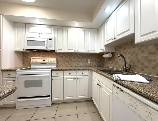 Kitchen featuring white cabinetry, speckled countertops, a mosaic tile backsplash, a built-in microwave, and a white electric range
