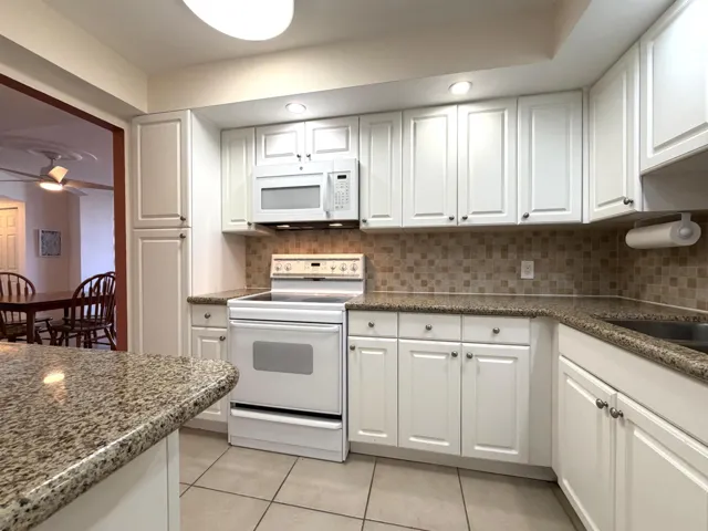 Contemporary kitchen featuring white cabinetry, granite-patterned countertops, and a tiled backsplash