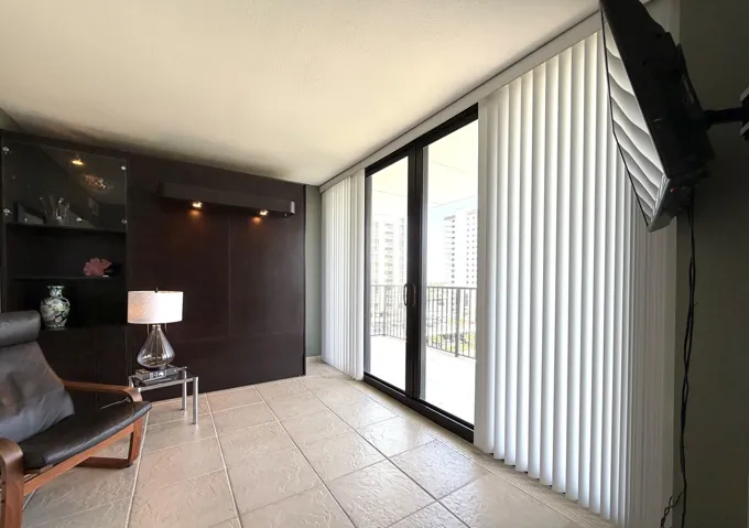 Glass sliding doors with vertical blinds, textured square tile flooring, and a built-in wall unit with display shelving and accent lighting