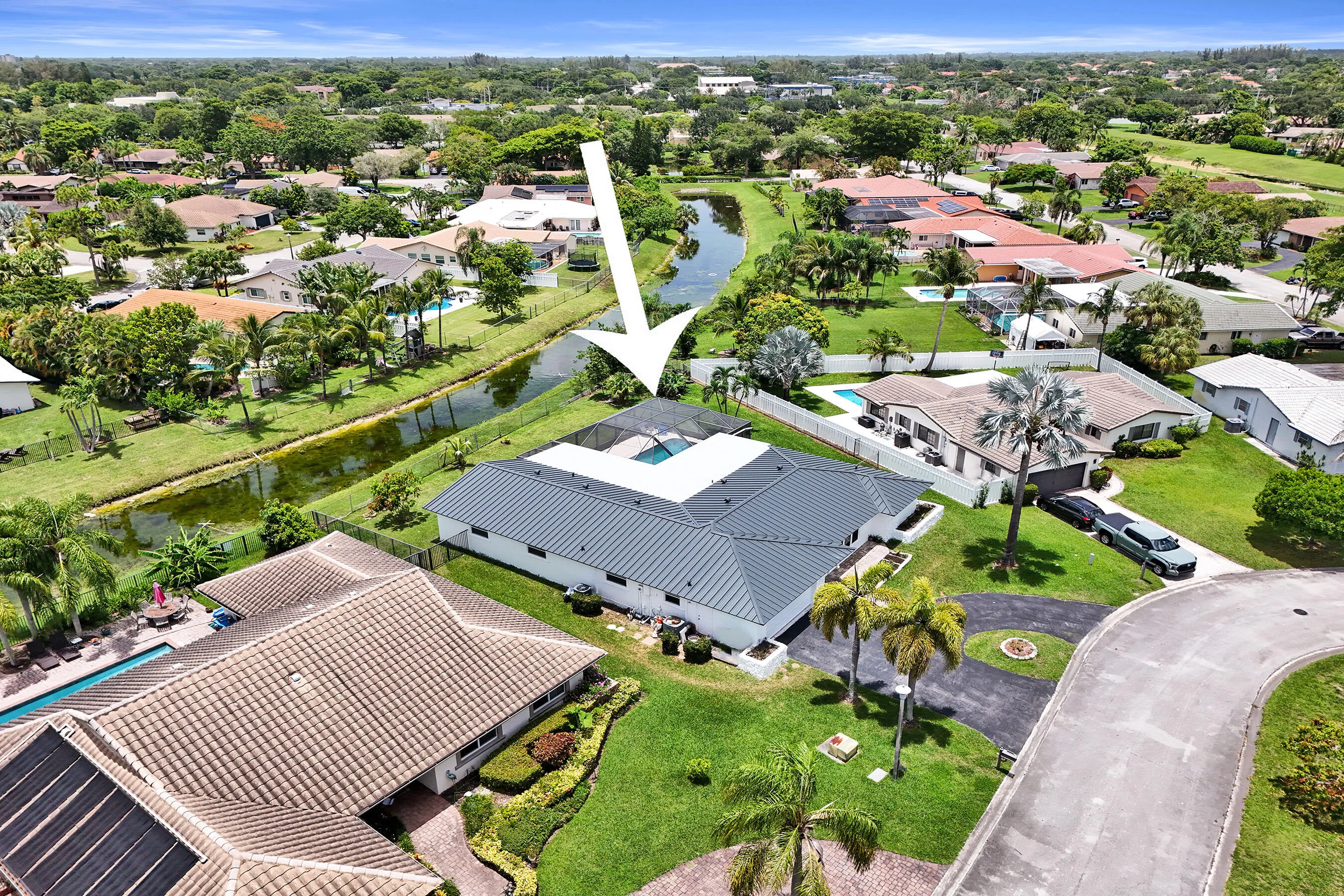 Aerial view of a residential property with a dark metal roof and white exterior, featuring a screened-in swimming pool