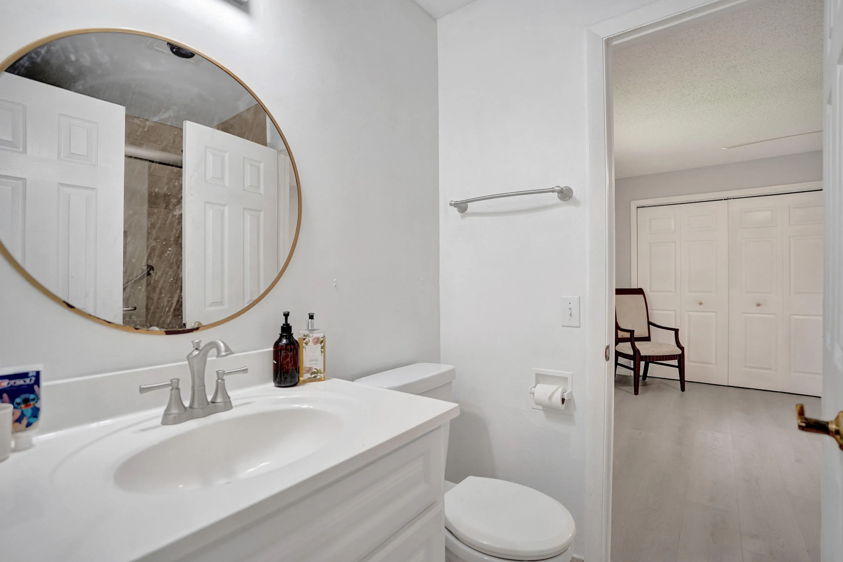 Bathroom featuring a white vanity with an integrated sink, brushed nickel faucet, and a round gold-framed mirror