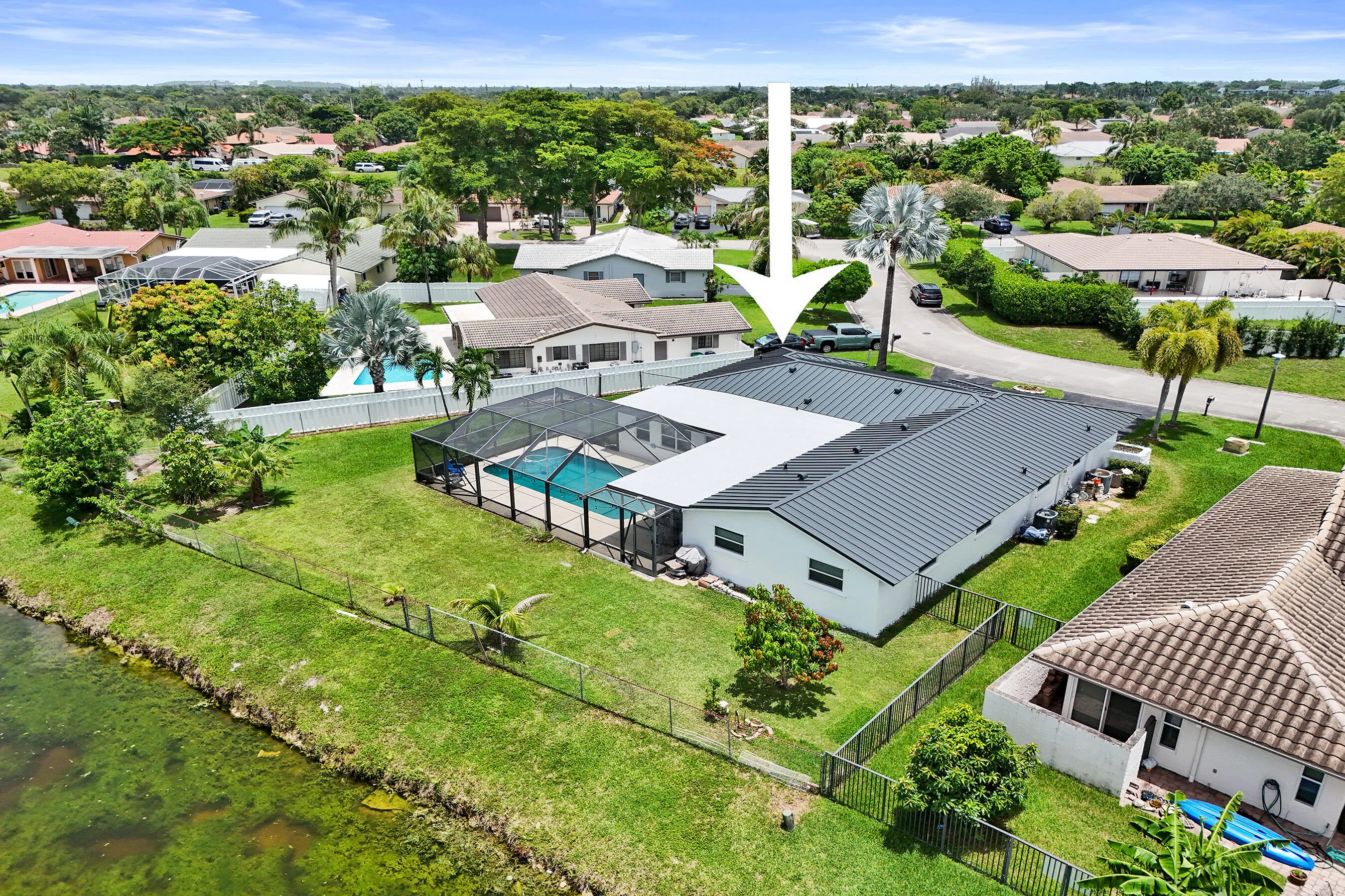 Expansive property featuring a screened-in swimming pool, a large green lawn, and mature palm trees