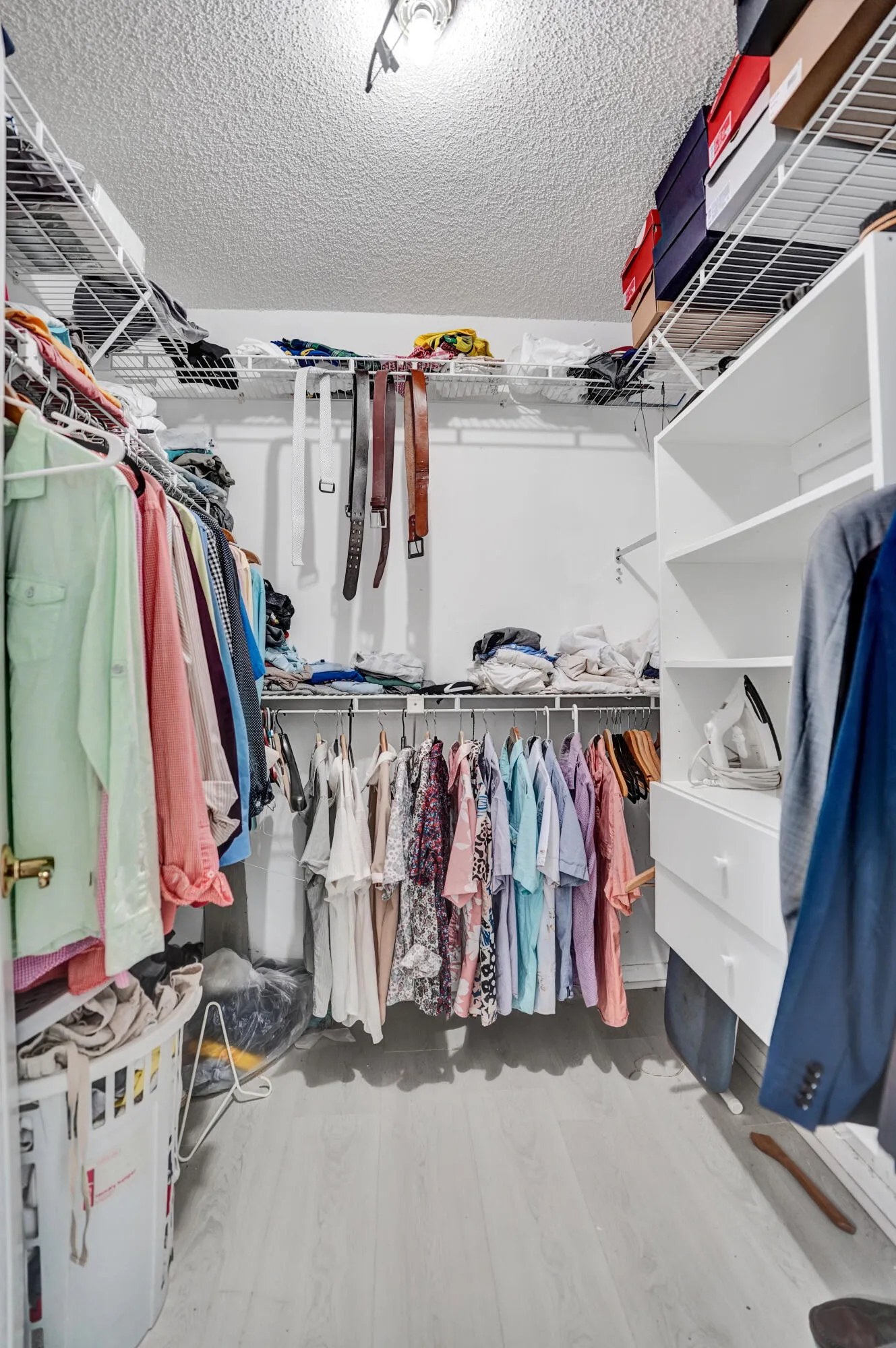 Walk-in closet featuring light wood-finish flooring, white wire shelving, built-in white cabinetry with drawers, and ceiling lighting