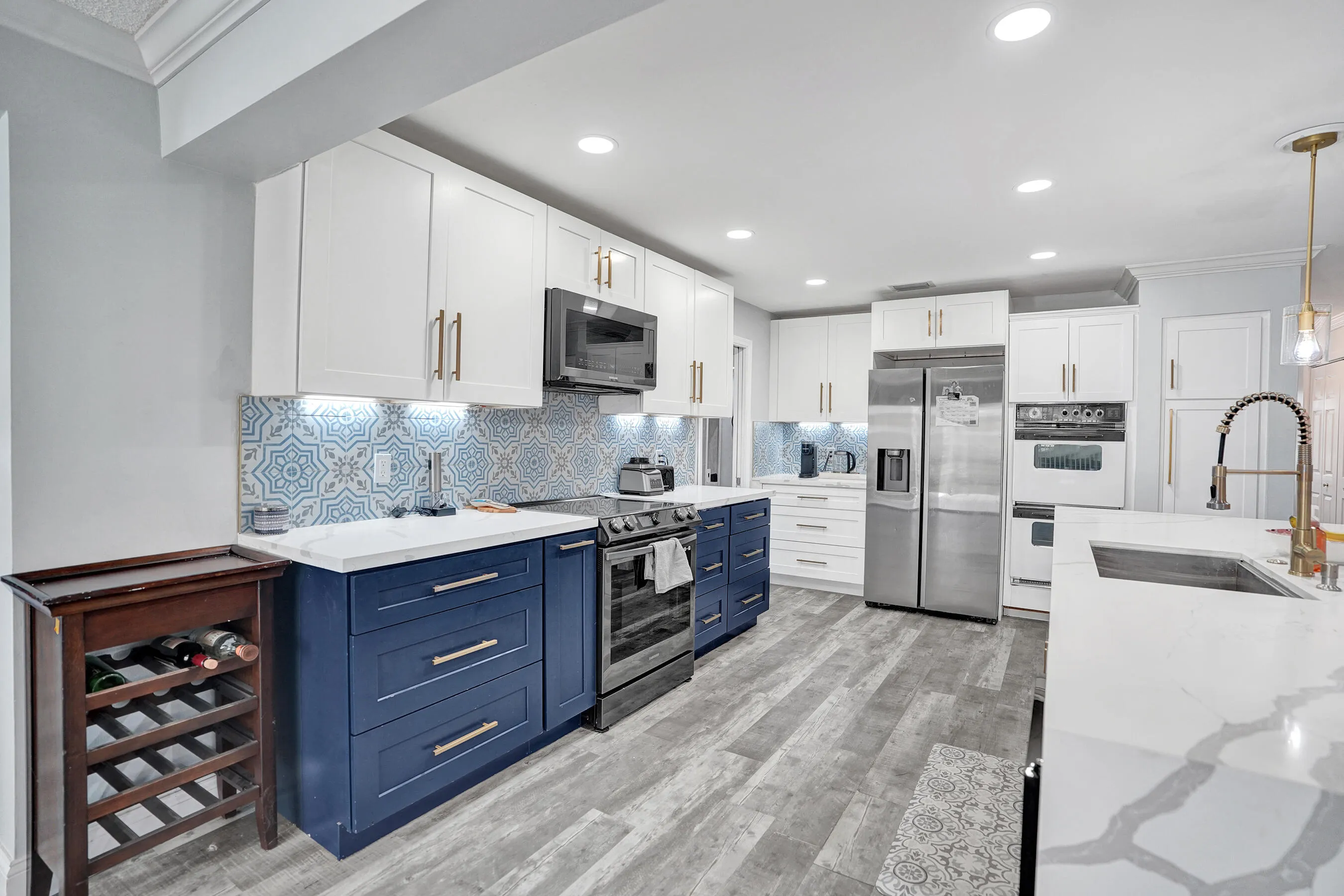 Spacious kitchen featuring two-tone cabinetry with white upper and navy lower cabinets, patterned tile backsplash, stainless steel appliances, and a central island with an undermount sink