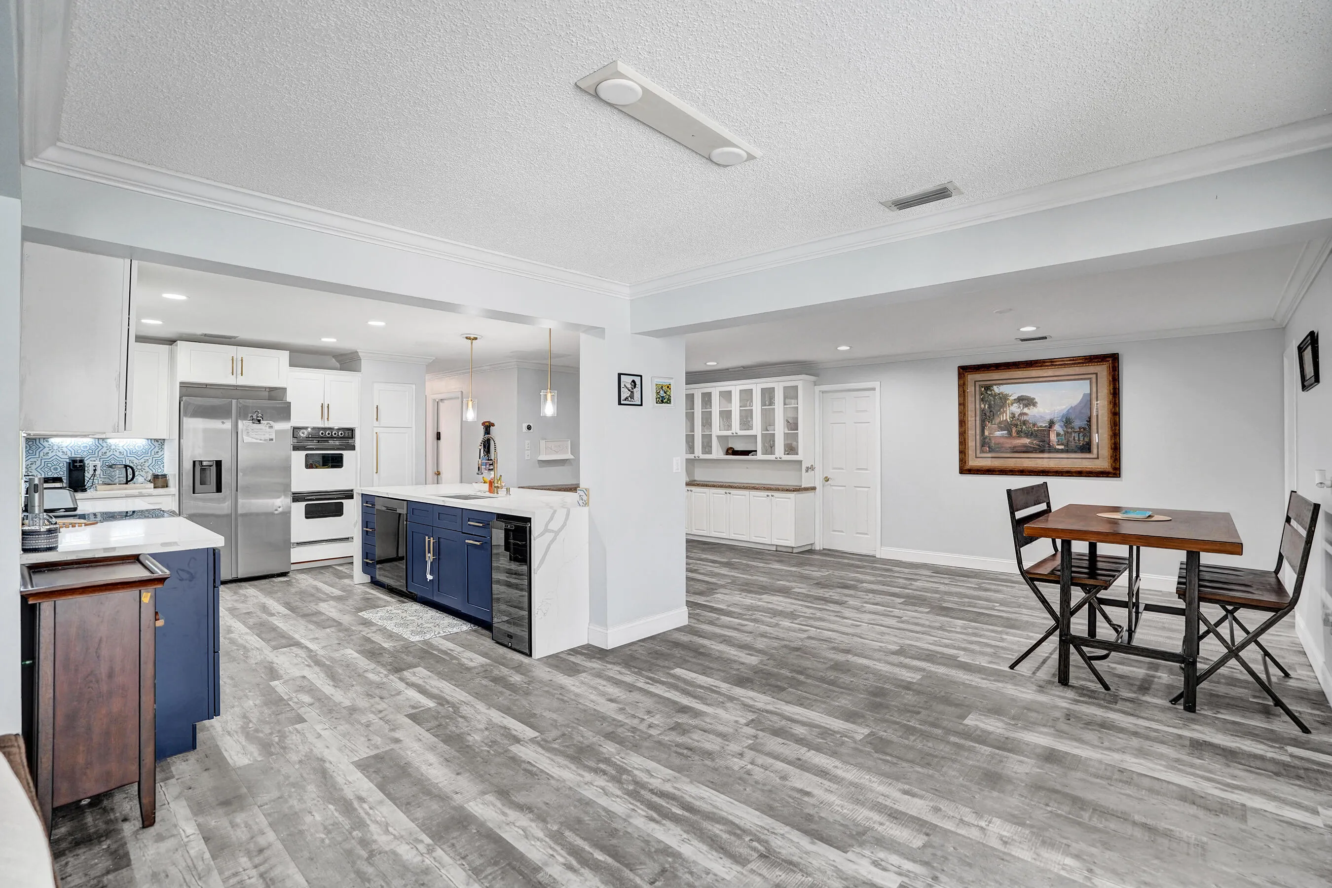 Open-concept kitchen featuring wood-finish flooring, white cabinetry, stainless steel appliances, and a central island with a built-in beverage refrigerator