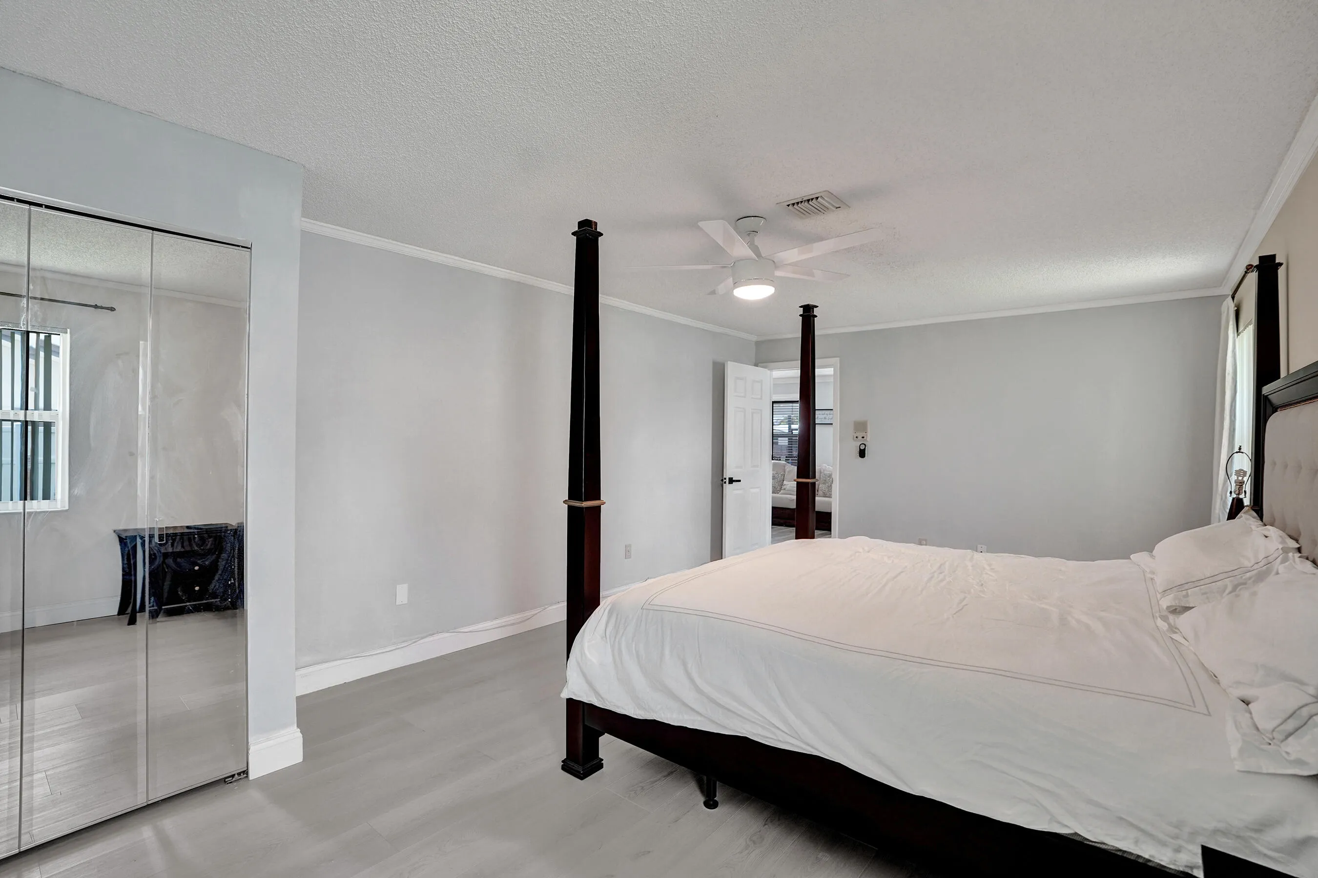 Spacious room featuring wood-finish flooring, mirrored closet doors, a ceiling fan with integrated lighting, and crown molding