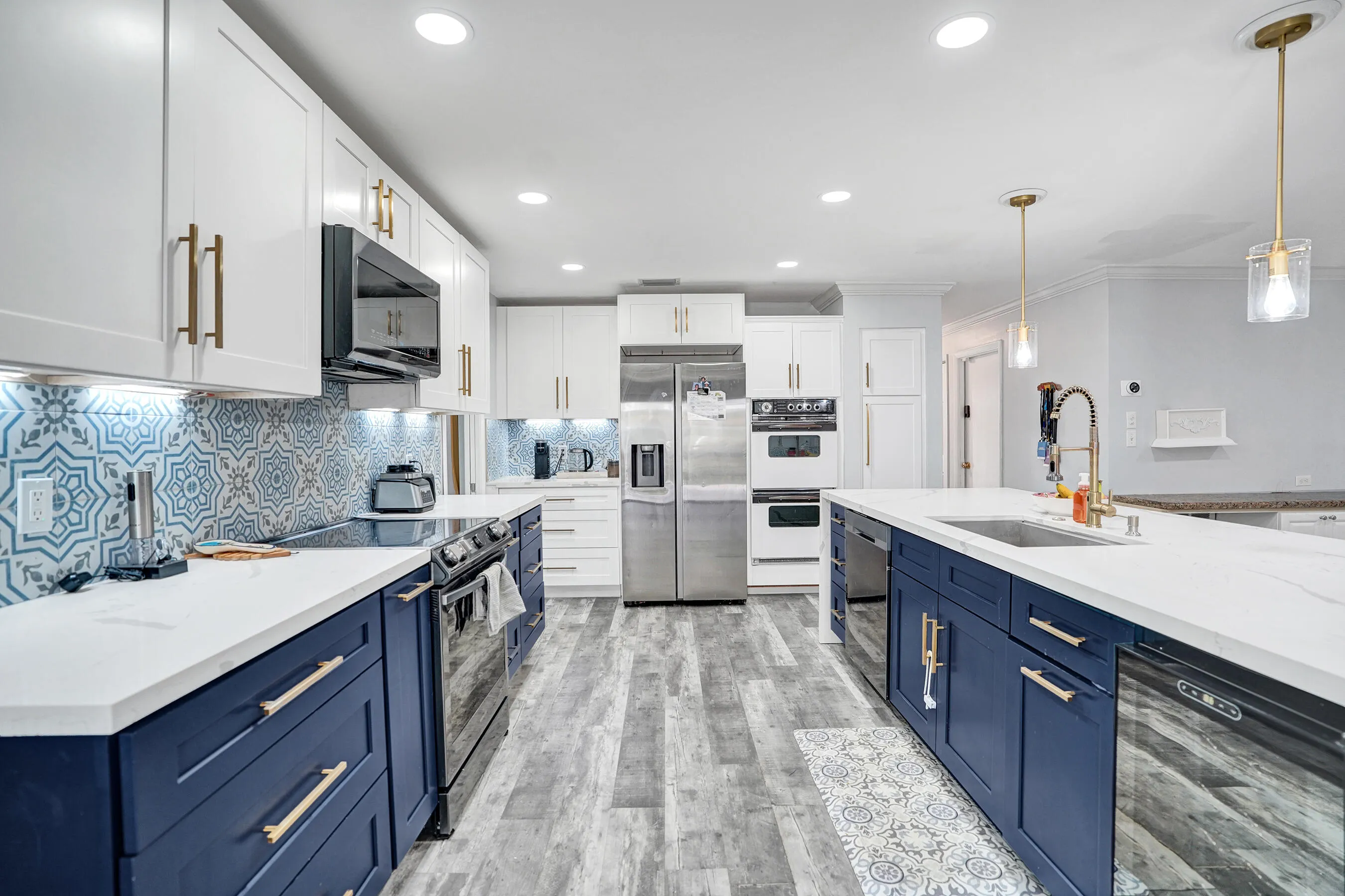Kitchen featuring dual-toned cabinetry with brass hardware, patterned tile backsplash, stainless steel appliances, and wood-finish flooring
