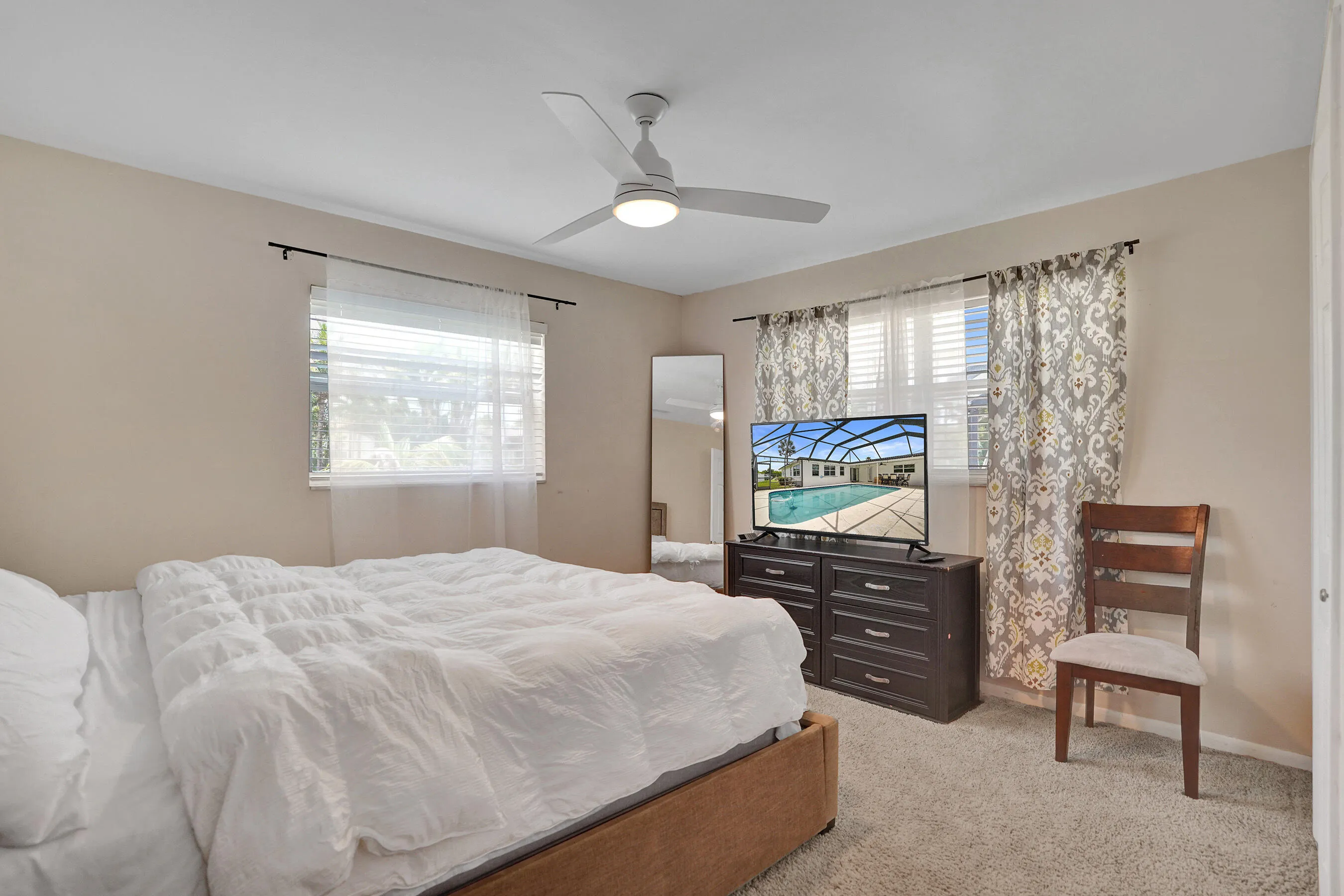 Carpeted room featuring a ceiling fan with integrated lighting, two windows with blinds, and decorative curtains