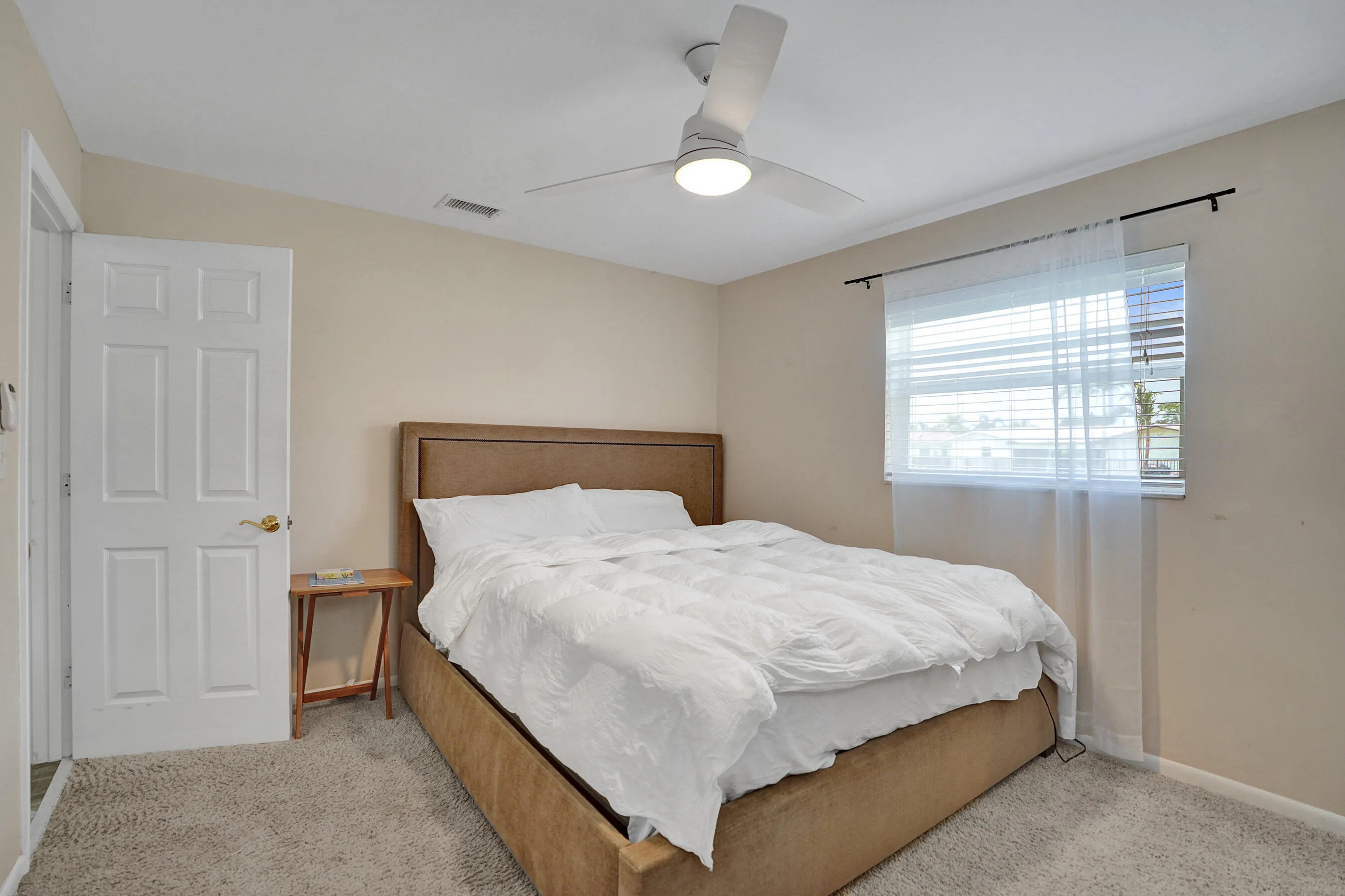 Inviting room featuring a modern ceiling fan with integrated lighting, textured carpet flooring, and a window with blinds and sheer curtains