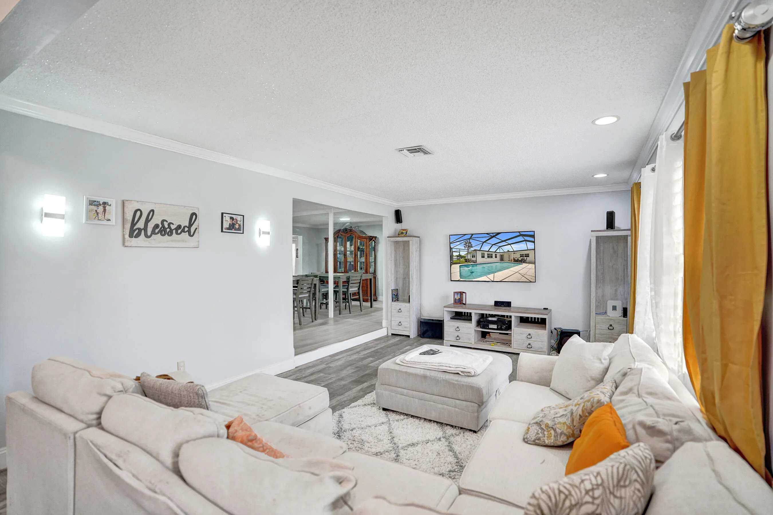 Spacious living area featuring light gray walls, crown molding, wood-finish flooring, and recessed ceiling lighting
