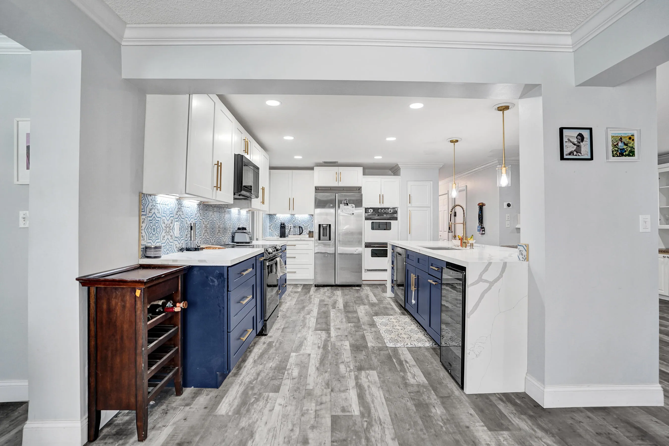 Open-concept kitchen featuring two-tone cabinetry, a patterned tile backsplash, stainless steel appliances, a center island with integrated sink, and wood-finish flooring