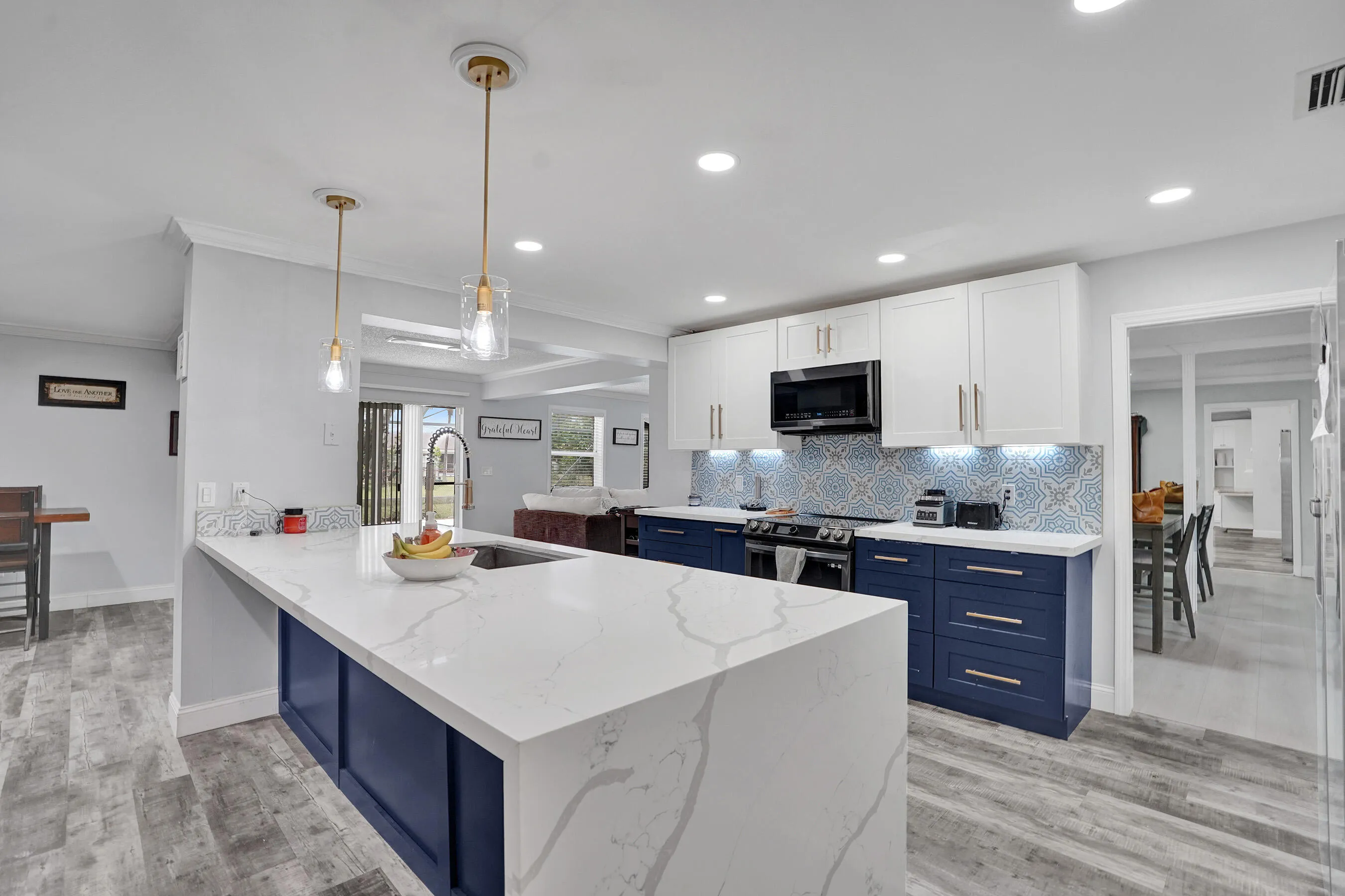 Kitchen featuring an extended island with a waterfall-edge countertop, two-tone cabinetry, and wood-finish flooring