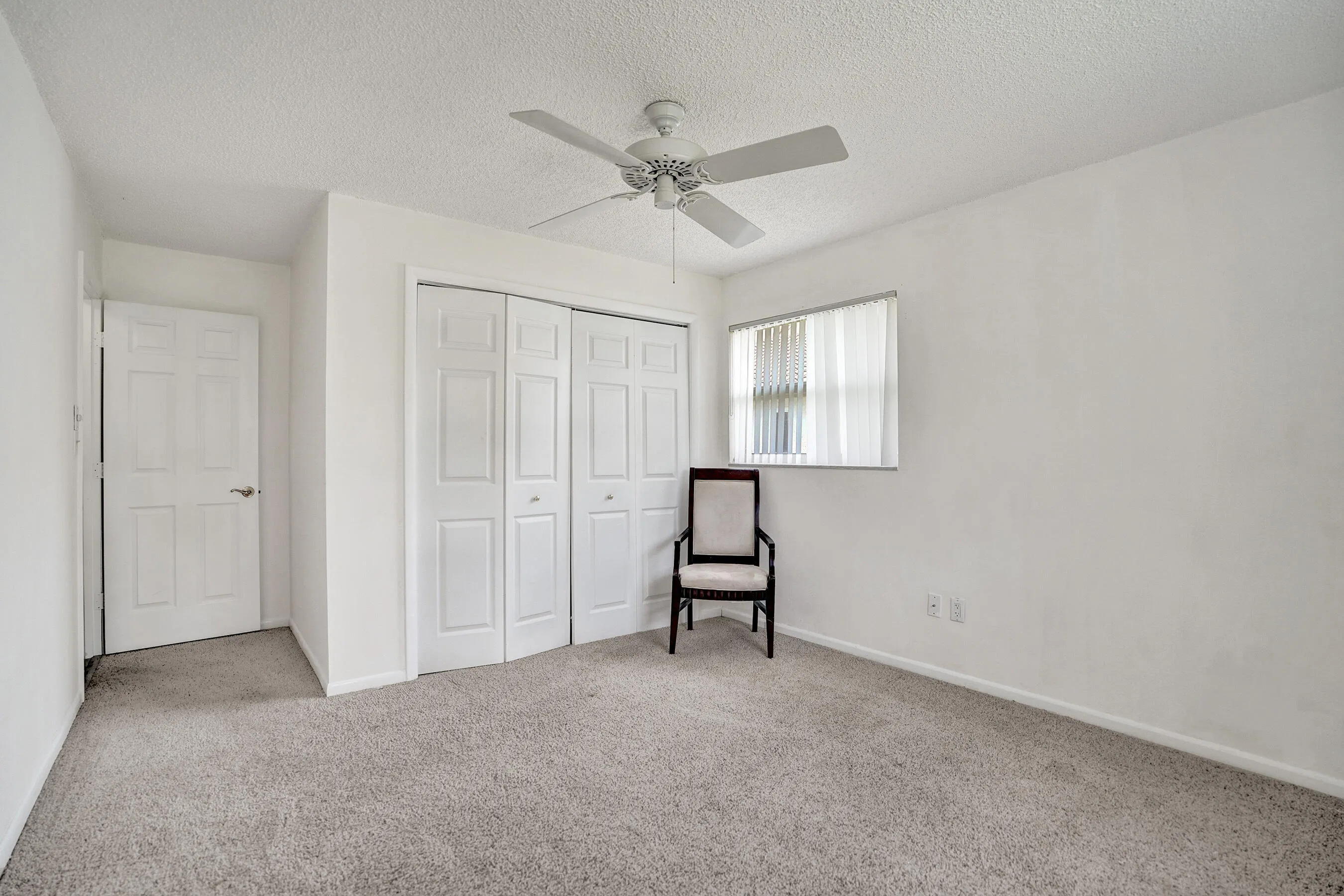 Carpeted room featuring a ceiling fan, bifold closet doors, a window with horizontal blinds, and a paneled entry door