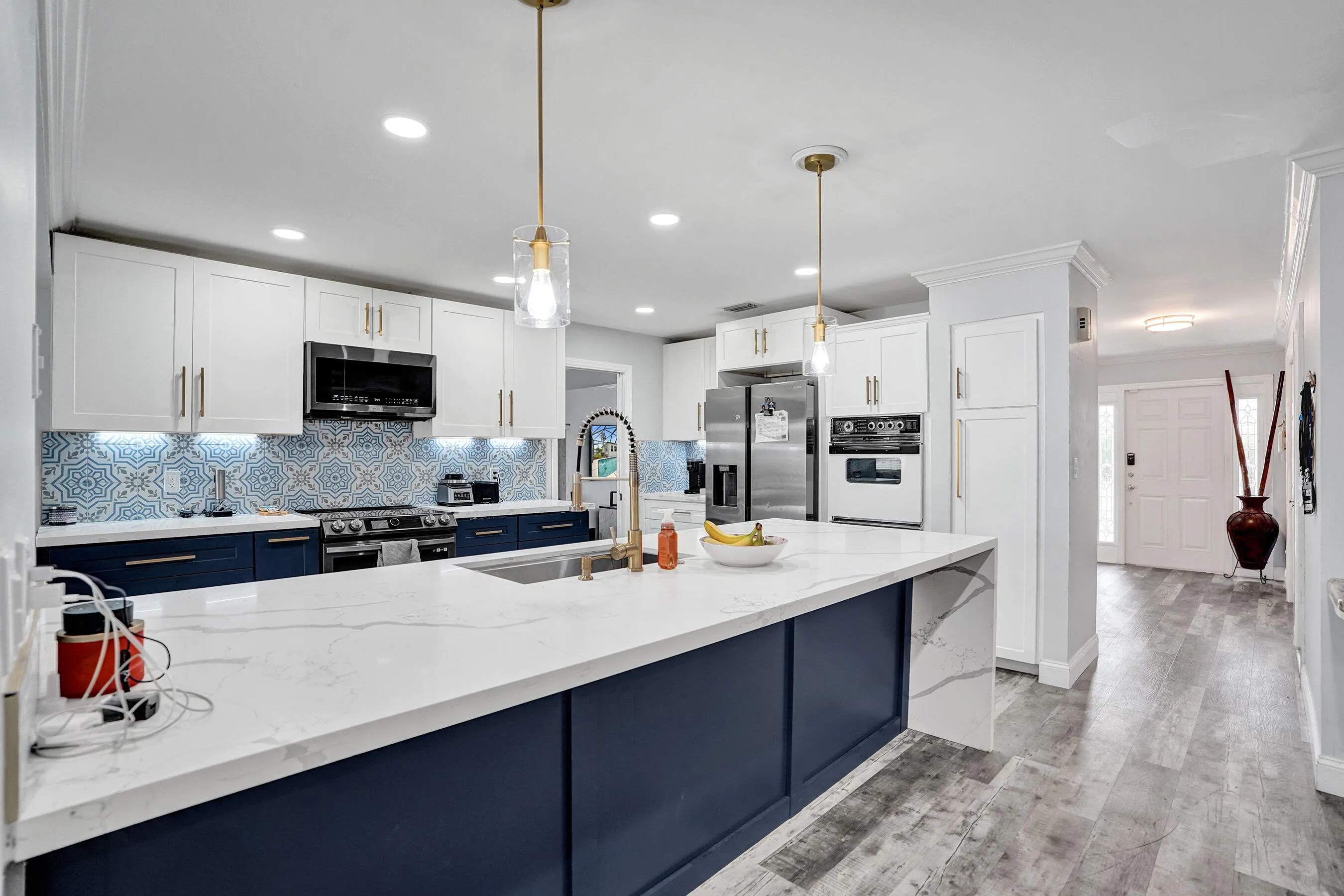 Modern kitchen featuring a large waterfall island with a sink, white upper cabinetry, navy lower cabinetry, and a patterned tile backsplash