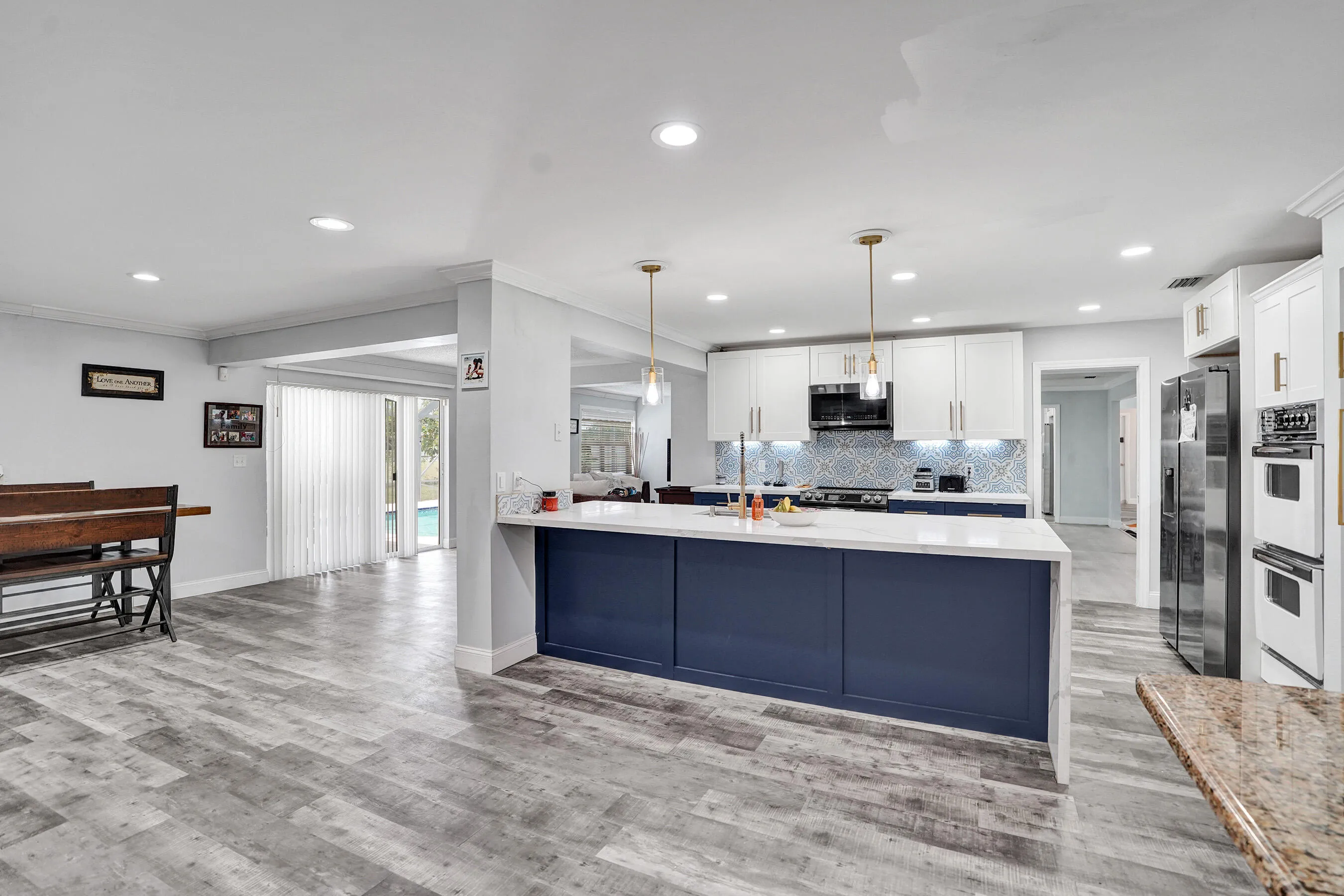 Open-concept kitchen featuring a large central island with a white countertop and navy cabinetry, stainless steel appliances, white upper cabinetry, and a patterned tile backsplash