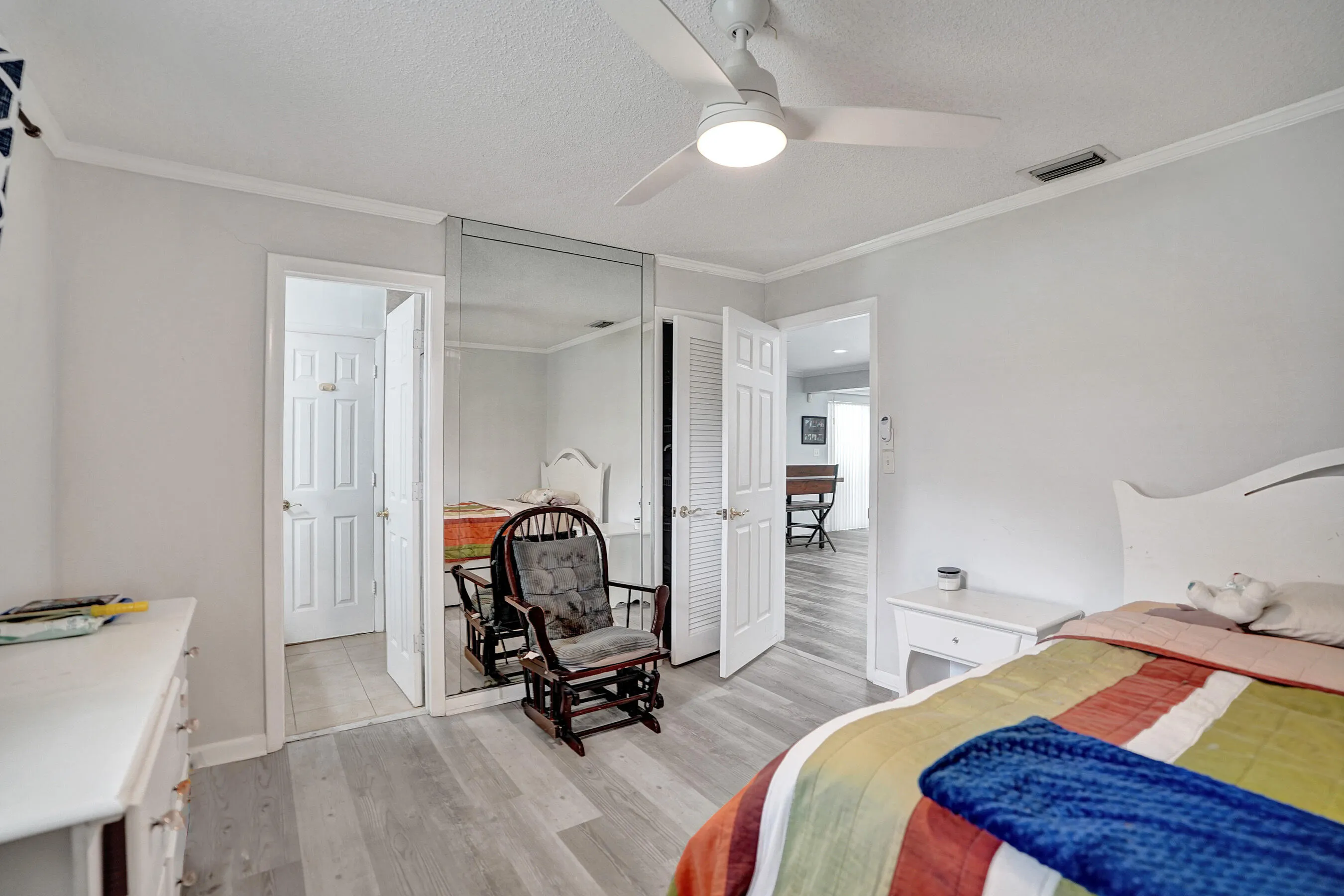 Bedroom featuring wood-finish flooring, a ceiling fan with integrated lighting, mirrored closet doors, and white trim