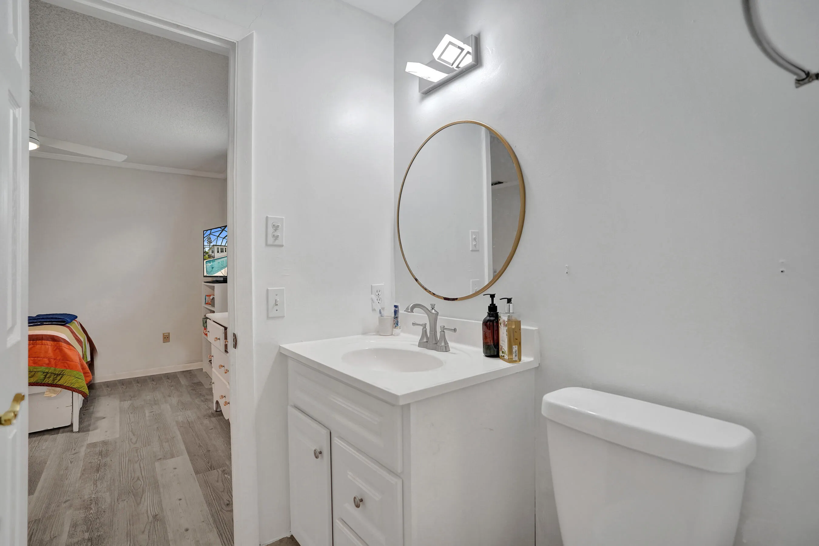 Bathroom featuring a white vanity with a single basin sink, a circular mirror with a gold-tone frame, and overhead vanity lighting