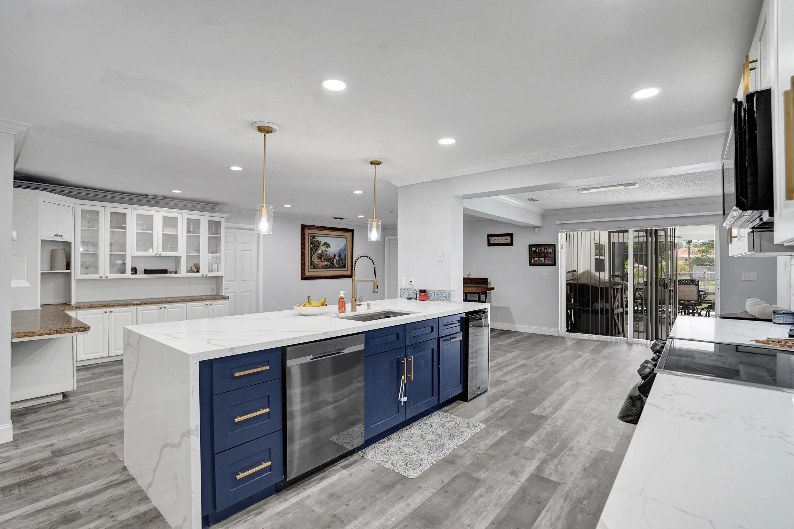 Spacious kitchen featuring a large central island with blue cabinetry and a white countertop, stainless steel appliances, recessed lighting, and wood-finish flooring