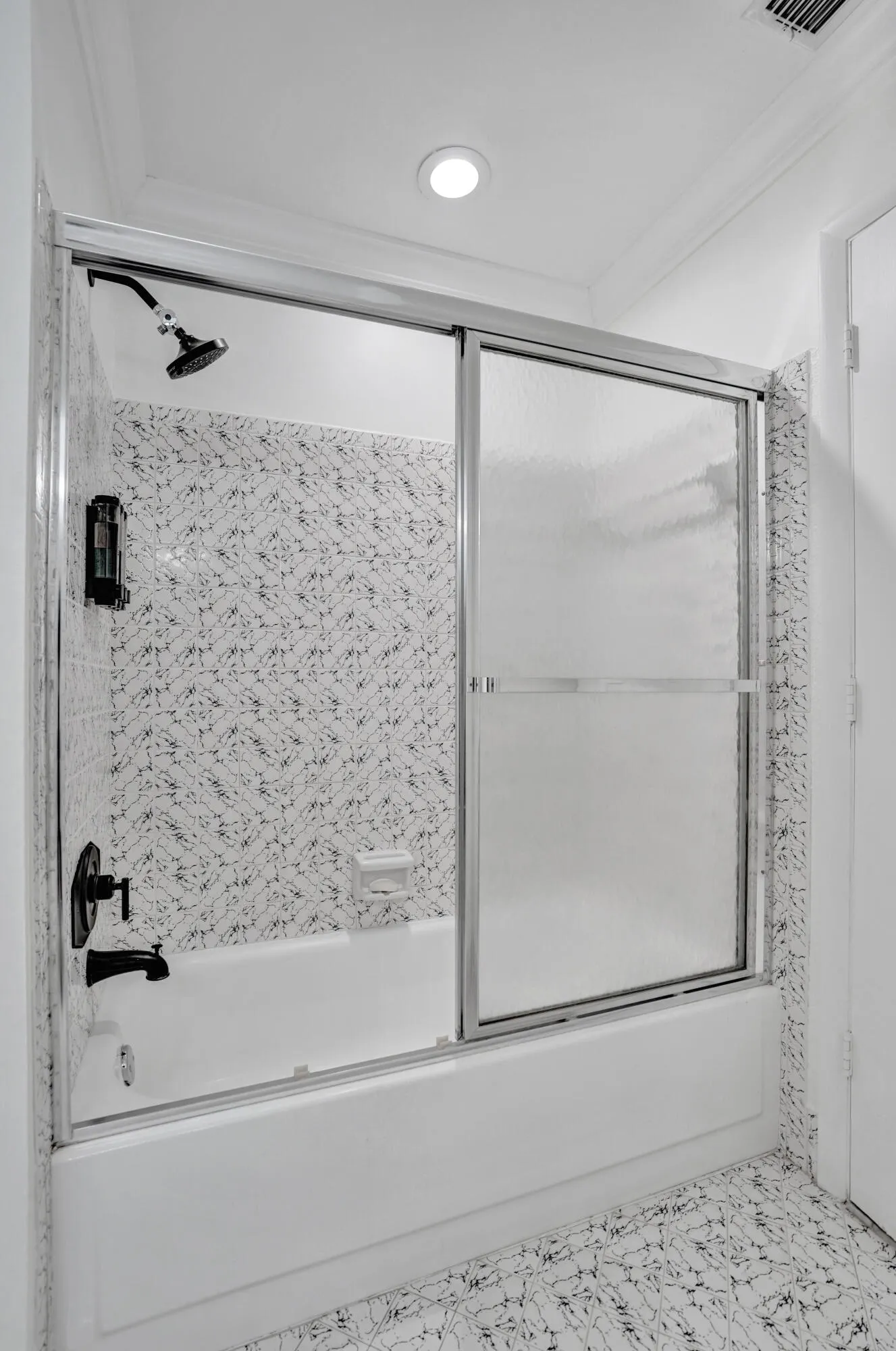 Bathtub with a sliding glass shower enclosure, matte black fixtures, and patterned wall tile