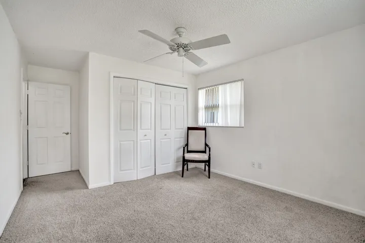 Carpeted room featuring a ceiling fan, bifold closet doors, a window with horizontal blinds, and a paneled entry door