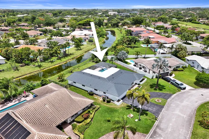 Aerial view of a residential property with a dark metal roof and white exterior, featuring a screened-in swimming pool