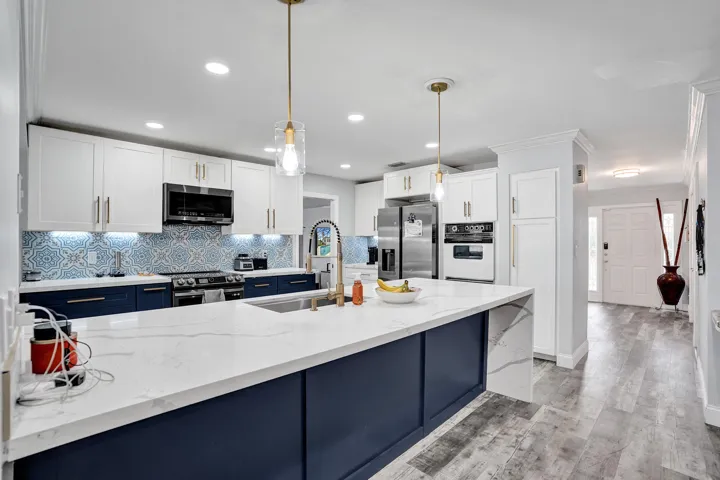 Modern kitchen featuring a large waterfall island with a sink, white upper cabinetry, navy lower cabinetry, and a patterned tile backsplash