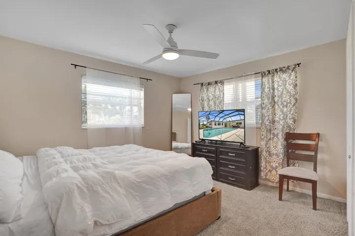 Carpeted room featuring a ceiling fan with integrated lighting, two windows with blinds, and decorative curtains