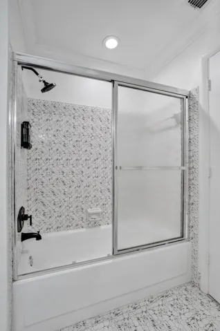Bathtub with a sliding glass shower enclosure, matte black fixtures, and patterned wall tile