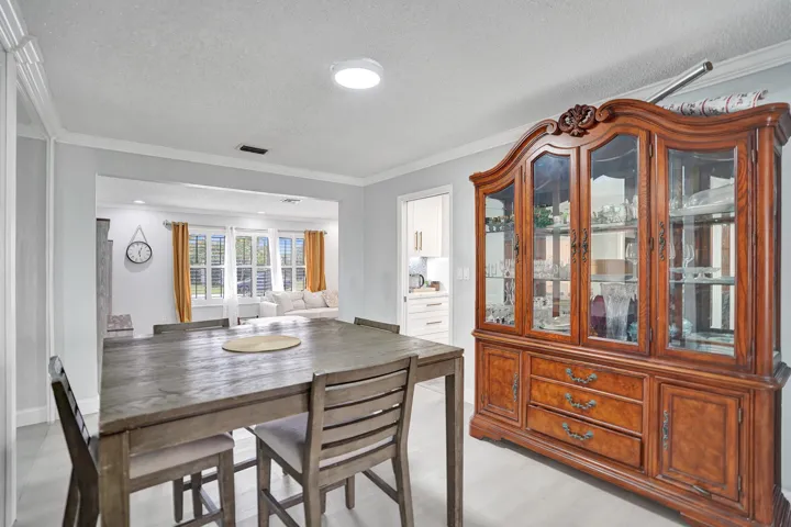 Spacious dining area featuring light-toned flooring, white crown molding, and an open entryway to an additional living space
