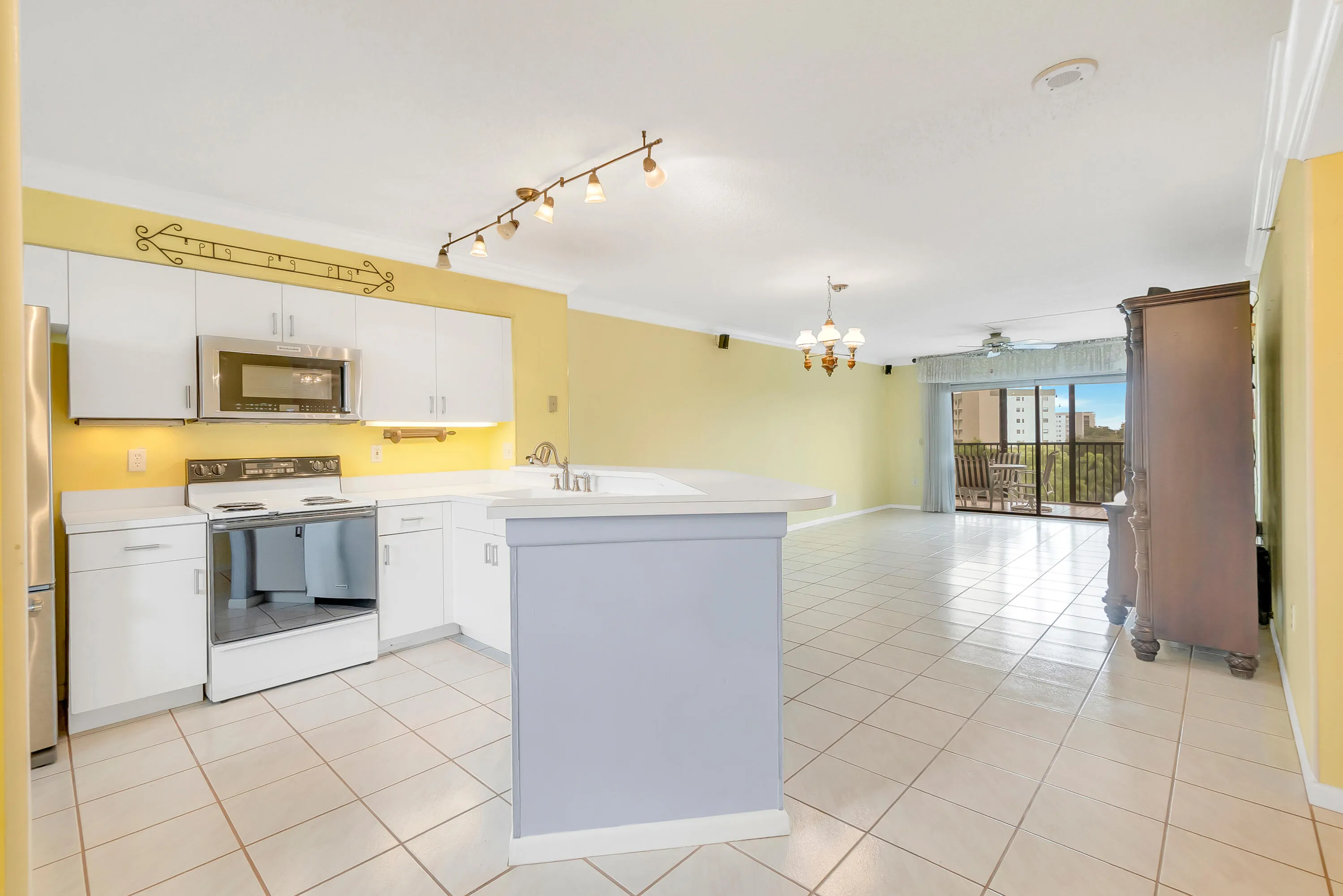 Open-concept living area with tile flooring throughout, featuring a kitchen with white cabinetry, stainless steel appliances, and a breakfast bar.