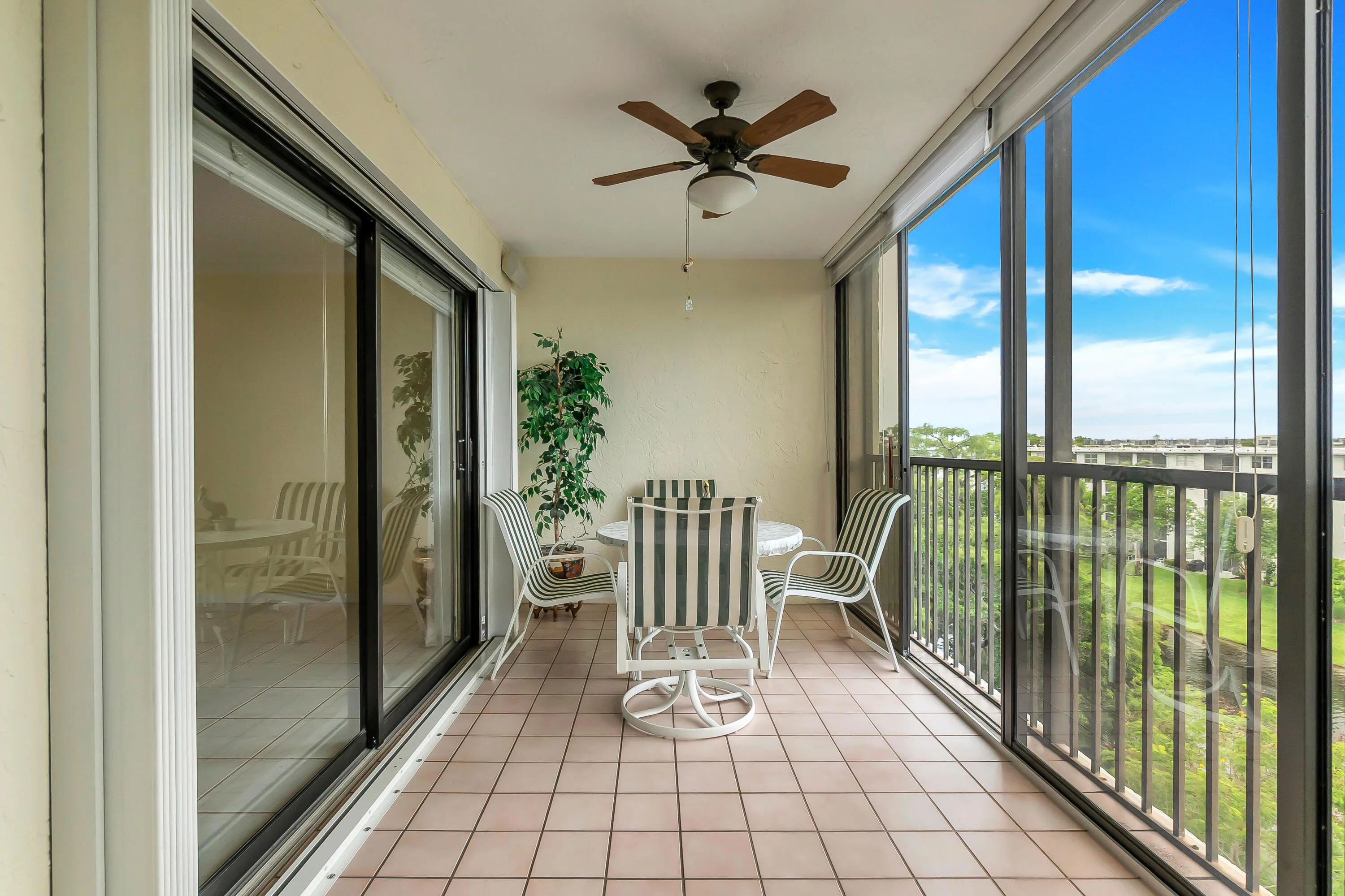 Enclosed balcony featuring light-toned tile flooring, a ceiling fan with integrated lighting, and expansive sliding glass panels offering substantial natural light. Full accordion hurricane shutters.
