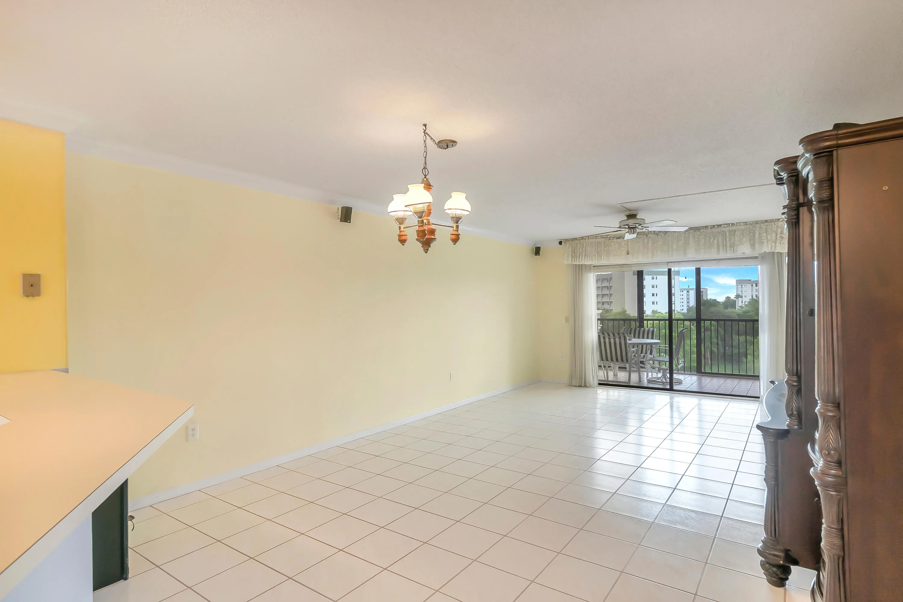 Spacious living/dining area featuring white tile flooring, a multi-light chandelier, a ceiling fan, and crown molding
