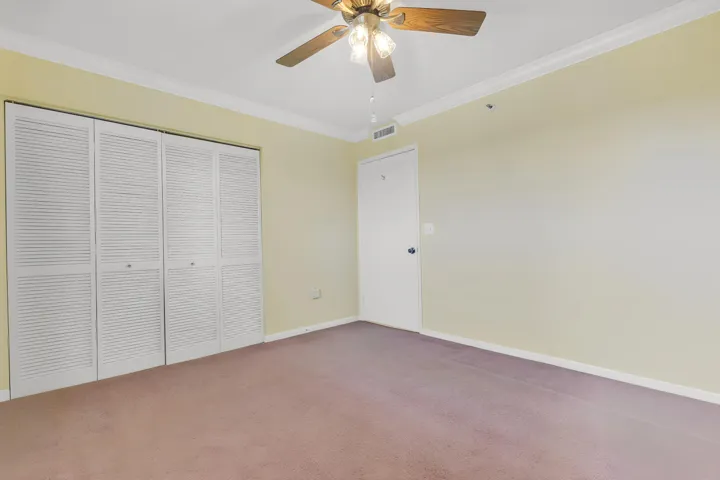 Guest/2nd bedroom featuring louvered bi-fold closet doors containing closet system, crown molding, a ceiling fan with light fixture, and a solid white door.