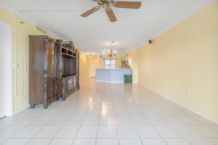 Expansive living-dining room featuring white tile flooring, crown molding, and a ceiling fan.